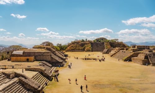 Tourists exploring Monte Alban, the ancient Zapotec archaeological site in Oaxaca, Mexico, under a clear blue sky.